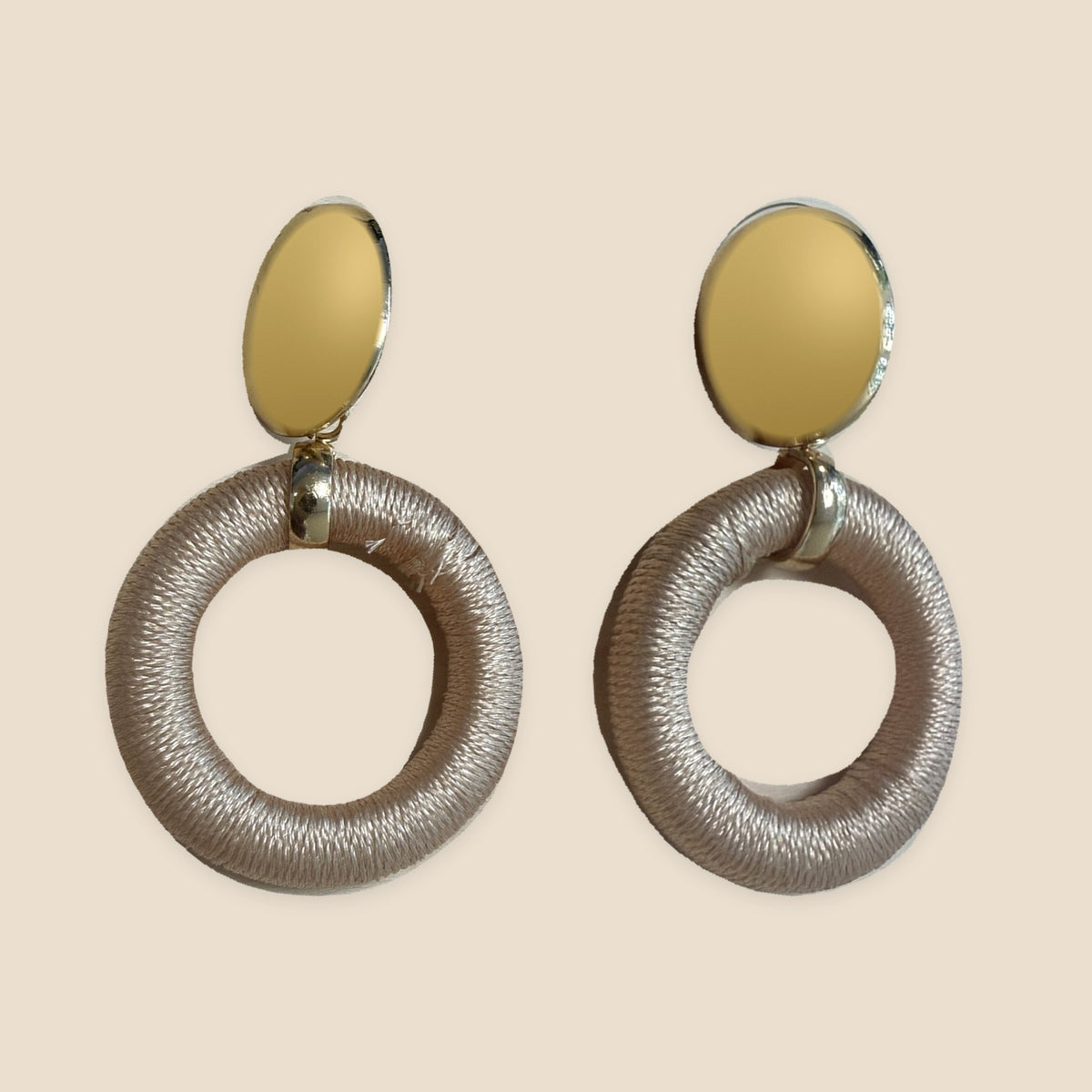Satin Halo champagnekleurige oorbellen recht naast elkaar op warm beige